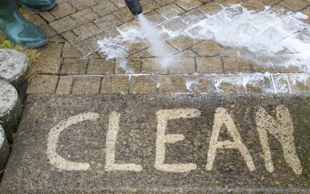 Pressure washer cleaning dirty pavement, revealing the word "CLEAN" on the surface.